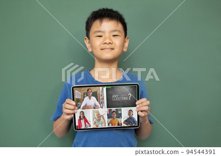 Smiling asian boy holding tablet for video call, with diverse elementary school pupils on screen Smiling asian boy holding tablet for video call, with diverse elementary school pupils on screen 94544391