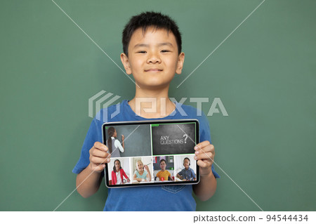 Smiling asian boy holding tablet for video call, with diverse elementary school pupils on screen Smiling asian boy holding tablet for video call, with diverse elementary school pupils on screen 94544434