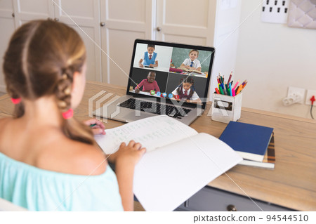 Caucasian girl using laptop for video call, with smiling diverse elementary school pupils on screen 94544510