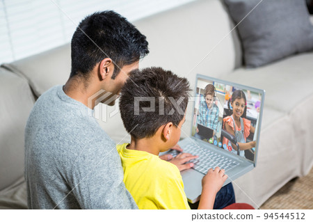 Biracial boy with father using laptop for video call, with elementary school pupils on screen 94544512