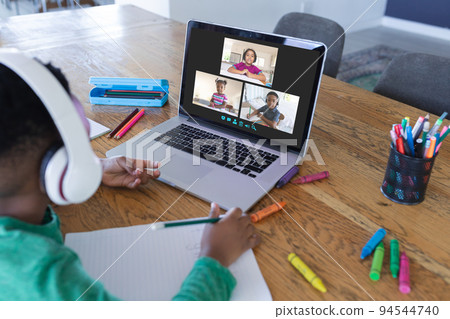 African american boy using laptop for video call, with diverse elementary school pupils on screen 94544740