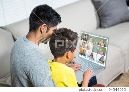 Biracial boy with father using laptop for video call, with elementary school pupils on screen 94544953