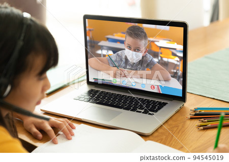 Asian girl using laptop for video call, with elementary school pupil with face mask on screen 94545019