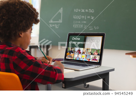 African american boy using laptop for video call, with diverse elementary school pupils on screen 94545249