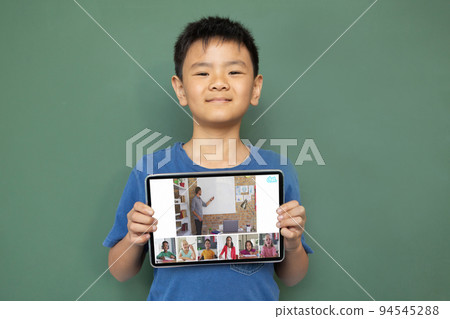 Smiling asian boy holding tablet for video call, with diverse elementary school pupils on screen Smiling asian boy holding tablet for video call, with diverse elementary school pupils on screen 94545288