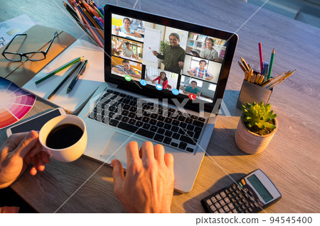 Hands of man using laptop for video call, with smiling diverse elementary school pupils on screen Hands of man using laptop for video call, with smiling diverse elementary school pupils on screen 94545400