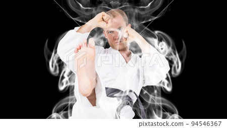 Composition of male martial artist over trails of smoke on black background Composition of male martial artist over trails of smoke on black background 94546367