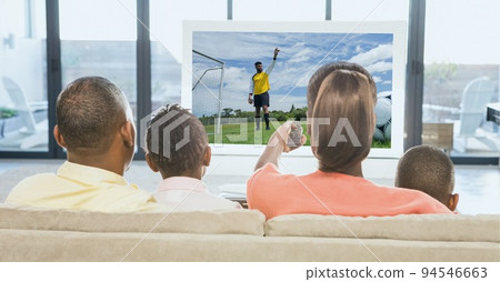 Composition of rear view of family of sports fans sitting on couch watching football match on tv Composition of rear view of family of sports fans sitting on couch watching football match on tv 94546663