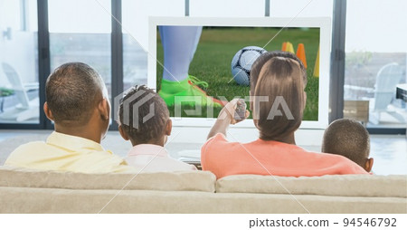Composition of rear view of family of sports fans sitting on couch watching football match on tv Composition of rear view of family of sports fans sitting on couch watching football match on tv 94546792