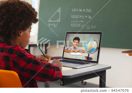 African american boy using laptop for video call, with biracial elementary school pupil on screen 94547076