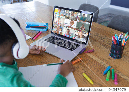 African american boy using laptop for video call, with diverse elementary school pupils on screen 94547079