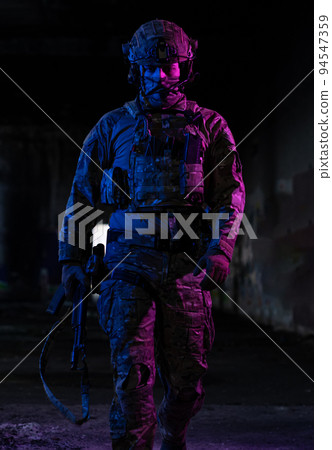 Army soldier in Combat Uniforms with an assault rifle and combat helmet night mission dark background. Blue and purple gel light effect. Army soldier in Combat Uniforms with an assault rifle and combat helmet night mission dark background. Blue and purple gel light effect. 94547359