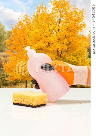 Man's hand in protective glove with bottle of dishwashing liquid. 94548509