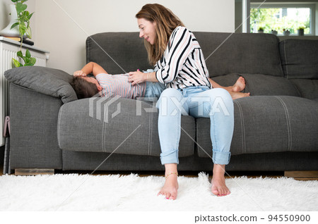 Loving mother tickling her little son on the sofa at home 94550900