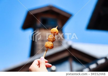 Woman's hand holding mitarashi dango while eating while walking around the old town 94552448