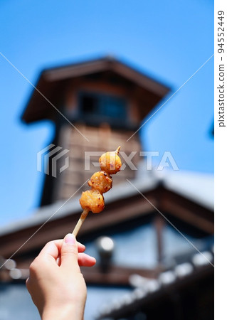 Woman's hand holding mitarashi dango while eating while walking around the old town Woman's hand holding mitarashi dango while eating while walking around the old town 94552449