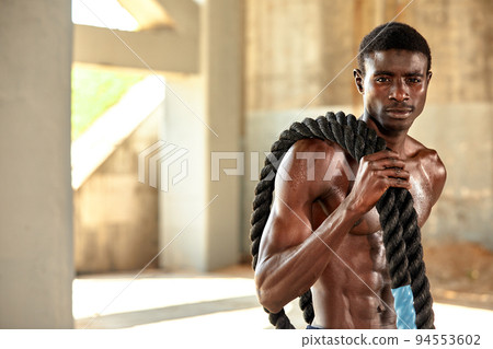 Rope workout. Sport man doing battle ropes exercise outdoor. Black male athlete exercising, doing functional fitness training with heavy rope Rope workout. Sport man doing battle ropes exercise outdoor. Black male athlete exercising, doing functional fitness training with heavy rope 94553602