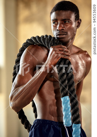 Rope workout. Sport man doing battle ropes exercise outdoor. Black male athlete exercising, doing functional fitness training with heavy rope 94553609