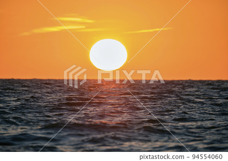 Ocean sunset. Big white sun on dramatic bright sky background, soft evening cloud over sea dark water 94554060