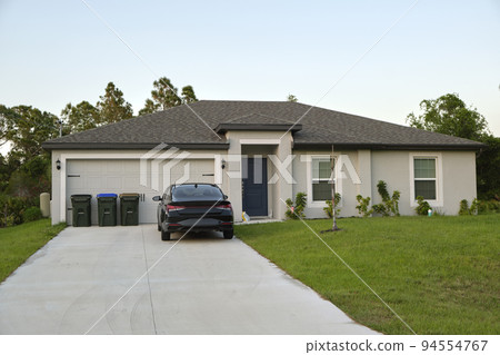 Car parked in front of wide garage double door on concrete driveway of new modern american house 94554767
