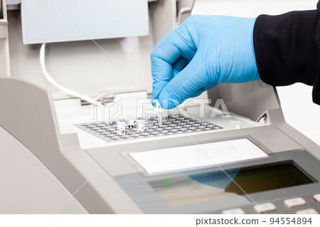 Closeup of a scientist hand while working at the laboratory with a thermal cycler. Polymerase chain reaction technique. PCR technique 94554894