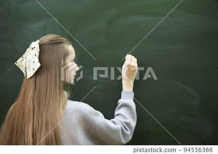 A teenage girl of middle school age writes with chalk on a blackboard. A teenage girl of middle school age writes with chalk on a blackboard. 94556366