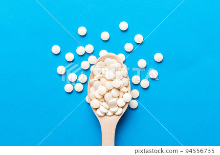 Heap of white pills on colored background. Tablets scattered on a table. Pile of red soft gelatin capsule. Vitamins and dietary supplements concept 94556735