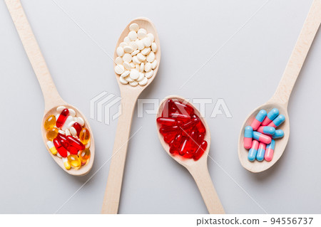 Vitamin capsules in a spoon on a colored background. Pills served as a healthy meal. Red soft gel vitamin supplement capsules on spoon 94556737