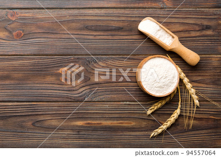 Flat lay of Wheat flour in wooden bowl with wheat spikelets on colored background. world wheat crisis Flat lay of Wheat flour in wooden bowl with wheat spikelets on colored background. world wheat crisis 94557064
