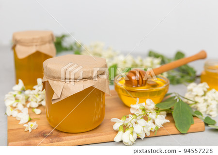 Sweet honey jar surrounded spring acacia blossoms. Honey flows from a spoon in a jar. jars of clear fresh acacia honey on wooden background 94557228