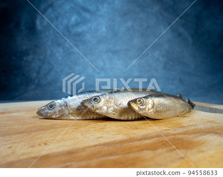 Lightly salted sprat on a cutting board. Whole small fish on the table. Lightly salted sprat on a cutting board. Whole small fish on the table. 94558633