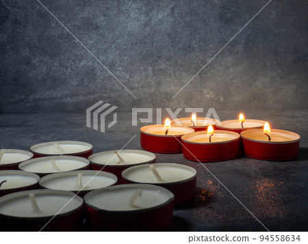 Short candles are burning on a dark background. Lots of small candles. Not all candles are lit. Short candles are burning on a dark background. Lots of small candles. Not all candles are lit. 94558634