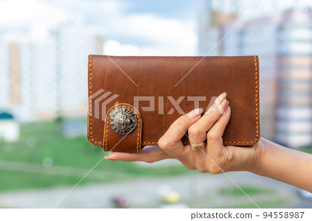Woman holds a brown natural leather wallet in her hand Woman holds a brown natural leather wallet in her hand 94558987