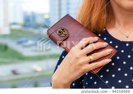 Woman holds a brown natural leather wallet in her hand 94558989