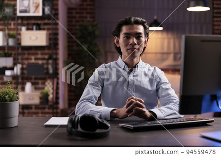 Asian man working remotely on computer, using online research information on website to plan business report. Doing remote work on startup company network, sending email to manager. 94559478