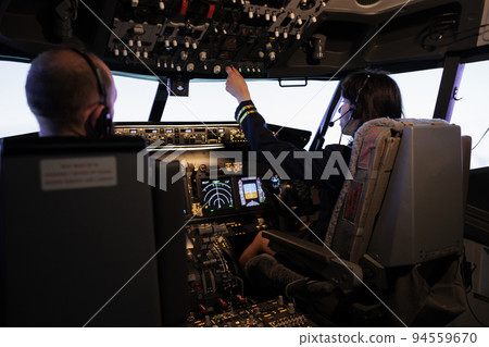 Female pilot assisting captain to takeoff and fly airplane, using buttons on dashboard command in pilot cockpit. Airliners flying plane jet with navigation windscreen and control panel. 94559670