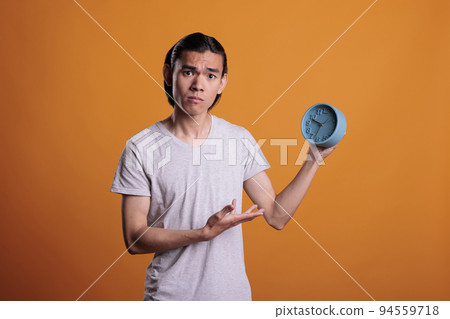 Young asian man running late, holding retro alarm, punctuality, deadline schedule, time management concept. Person overslept in morning, anxious teenager pointing at vintage clock Young asian man running late, holding retro alarm, punctuality, deadline schedule, time management concept. Person overslept in morning, anxious teenager pointing at vintage clock 94559718