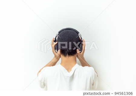 [Japan] Back view of a man listening to music with both hands on headphones in front of a white wall 94561306