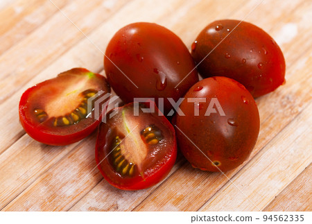 Whole and sliced ripe brownish mini tomatoes on table 94562335