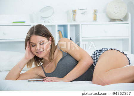 Portrait of young sexy woman lying with smartphone in bed Portrait of young sexy woman lying with smartphone in bed 94562597