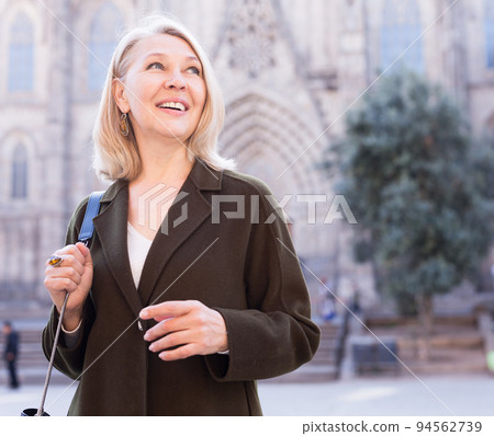 Portrait of mature cheerful woman standing on a old city street Portrait of mature cheerful woman standing on a old city street 94562739