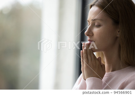 Serious calm pretty adult woman standing at window indoors Serious calm pretty adult woman standing at window indoors 94566901