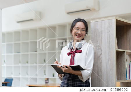 Young female student doing assignments in library. Asian woman taking notes from textbooks. Young female student doing assignments in library. Asian woman taking notes from textbooks. 94566902