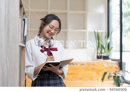 Young female student doing assignments in library. Asian woman taking notes from textbooks. Young female student doing assignments in library. Asian woman taking notes from textbooks. 94566906