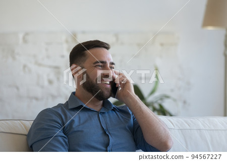 Happy millennial man talks on smartphone at home Happy millennial man talks on smartphone at home 94567227