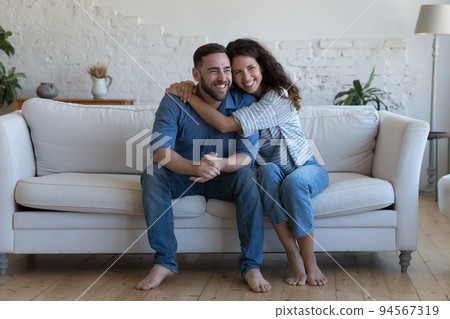 Romantic couple hugging seated on sofa at home Romantic couple hugging seated on sofa at home 94567319