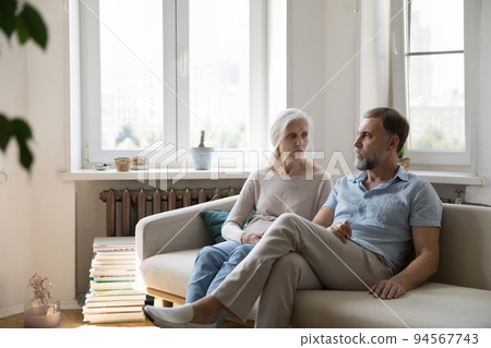 Serious concerned senior couple talking on home couch Serious concerned senior couple talking on home couch 94567743
