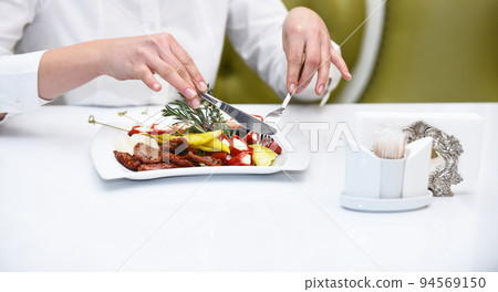 Female hands with knife and fork cutting pickled pepper Female hands with knife and fork cutting pickled pepper 94569150