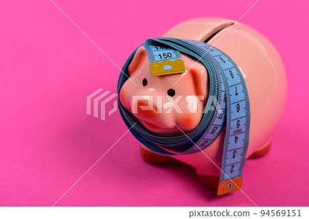 Piggy bank tied with measuring tape. Budget and squeezed savings Piggy bank tied with measuring tape. Budget and squeezed savings 94569151