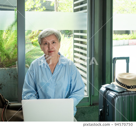 relax, vacation, travel, portrait of senior adult elderly asian woman 60s smiling using the computer laptop while waiting for her travel time. 94570750